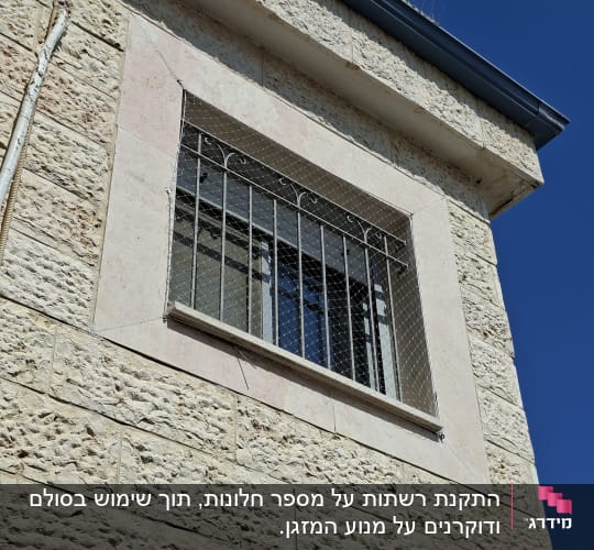 חלון עם רשת ומחסום יונים על קיר אבן